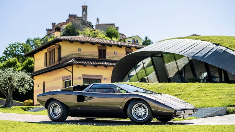 A lamborgini Countach parked outside of a classic itallian home and a futuristic home on a sunny day
