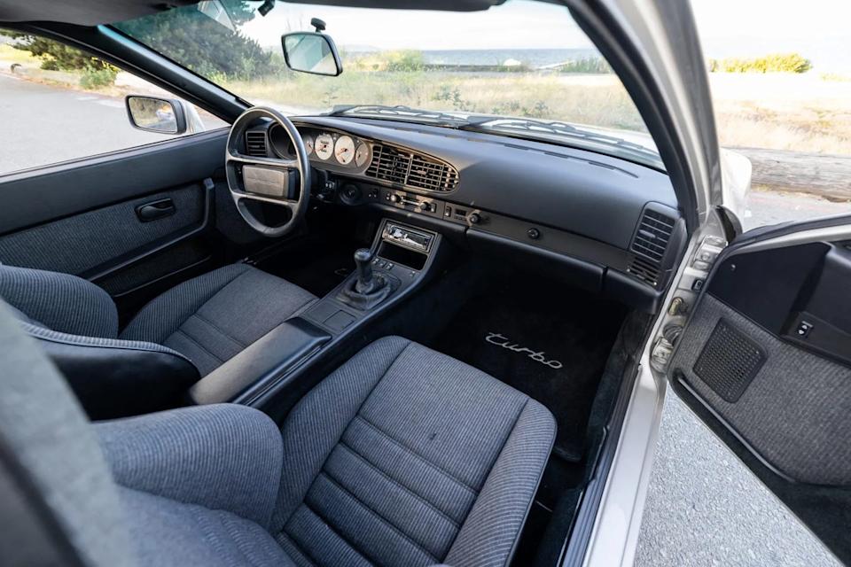 interior view from driver side showing gray cloth seats, manual gearshift, and black dashboard.