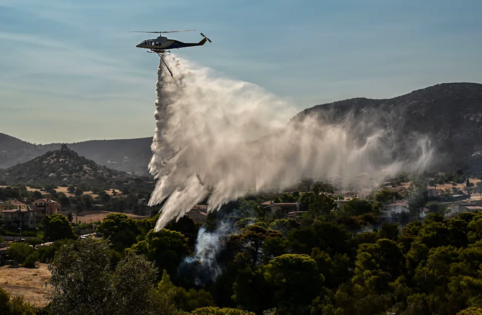 A firefighting helicopter drops water over a burned area.