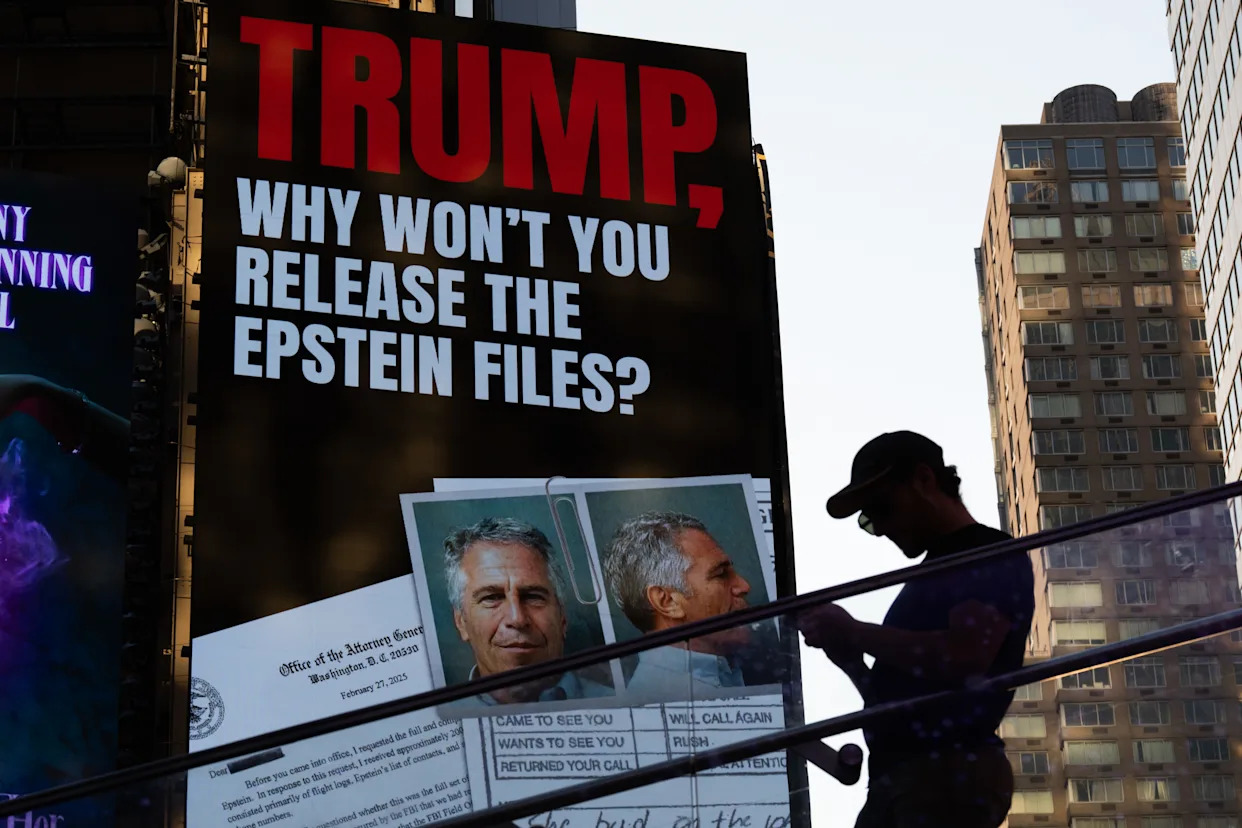 A large black billboard reads &#x00201c;Trump, why won&#x002019;t you release the Epstein files?&#x00201d; while a man in a baseball cap stands in front of it.
