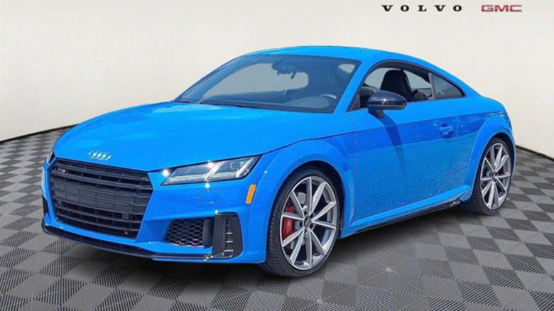 a bright blue Audi TT parked in a non-descript room on a diamond patterned floor.