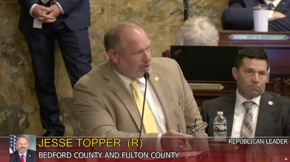 A man in a suit is speaking at a podium during a political session. A nameplate reads "Jesse Topper, Republican Leader for Bedford County and Fulton County."