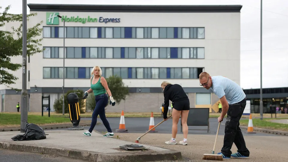 Three people are pictured outside the hotel. Two are holding brooms and seem to be cleaning the ground.