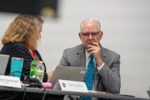  Nebraska Education Commissioner Brian Maher of Lincoln talks to a staffer from the Nebraska Department of Education during the first meeting of the School Financing Review Commission. Aug. 12, 2025. (Zach Wendling/Nebraska Examiner)