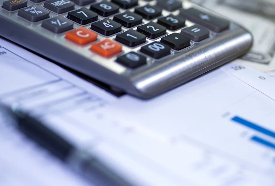 Calculator on financial documents with graphs, pen, glasses, and dollar bills, depicting financial planning or budgeting