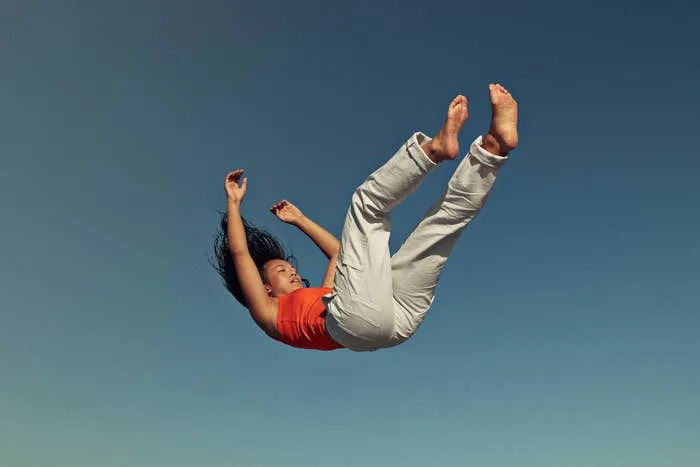 Person joyfully falling or jumping in mid-air, wearing casual clothing against a clear sky background