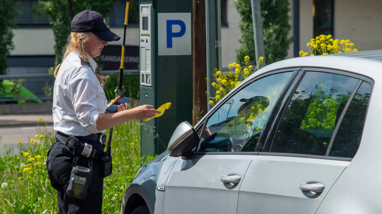 A parking enforcement officer writes a ticket for illegal parking