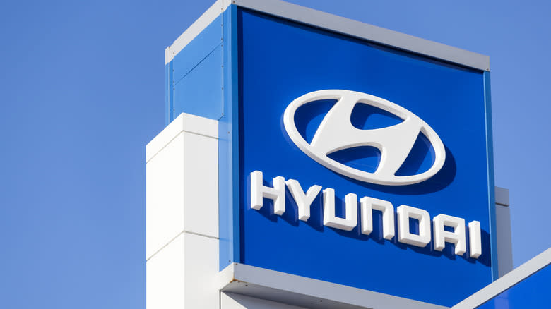Hyundai sign and logo above car dealership lot over building and showroom with clear, blue sky in background.