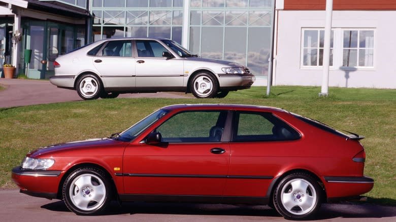 A red Saab 900 coupe parked in front of a silver Saab 900 five-door parked in front of a building