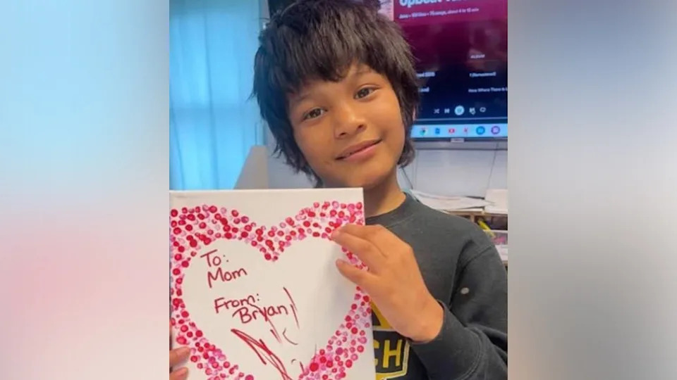 Bryan Vasquez posing with a heart-shaped card that reads: "To Mom, From Bryan"