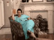 Person in a flowing gown sits leisurely in a patterned chair, holding a phone by their ear, looking relaxed and conversational