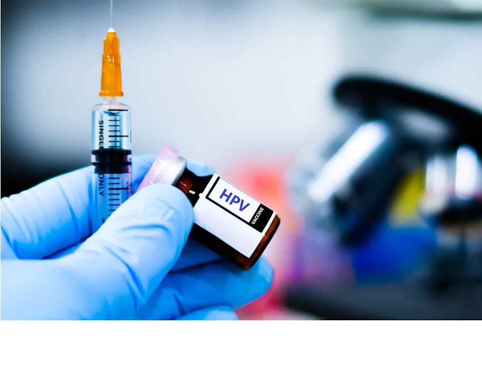 A gloved hand holds an HPV vaccine vial and syringe, ready for administration, against a blurred background