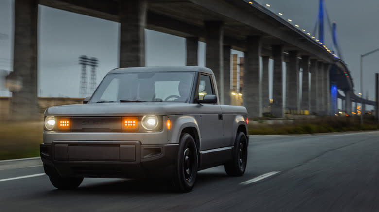 a gray Slate pickup driving past a bridge at dusk with its lights on