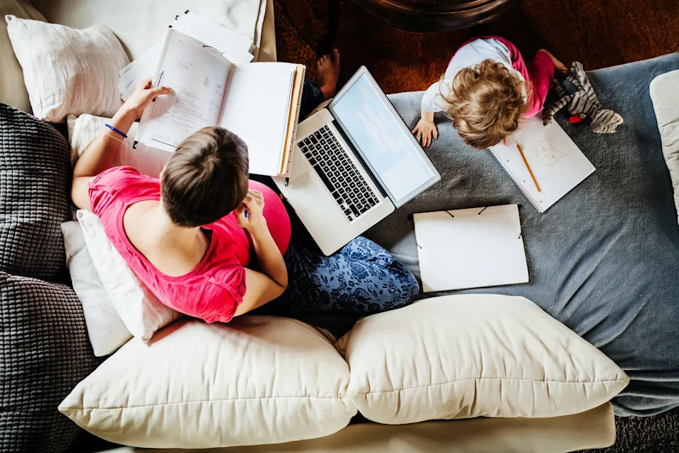 Aerial stock photo of a woman working at home with her child playing next to her.