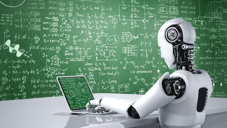 A white, shiny, futuristic robot types on a laptop computer in front of a green chalkboard with equations written on it