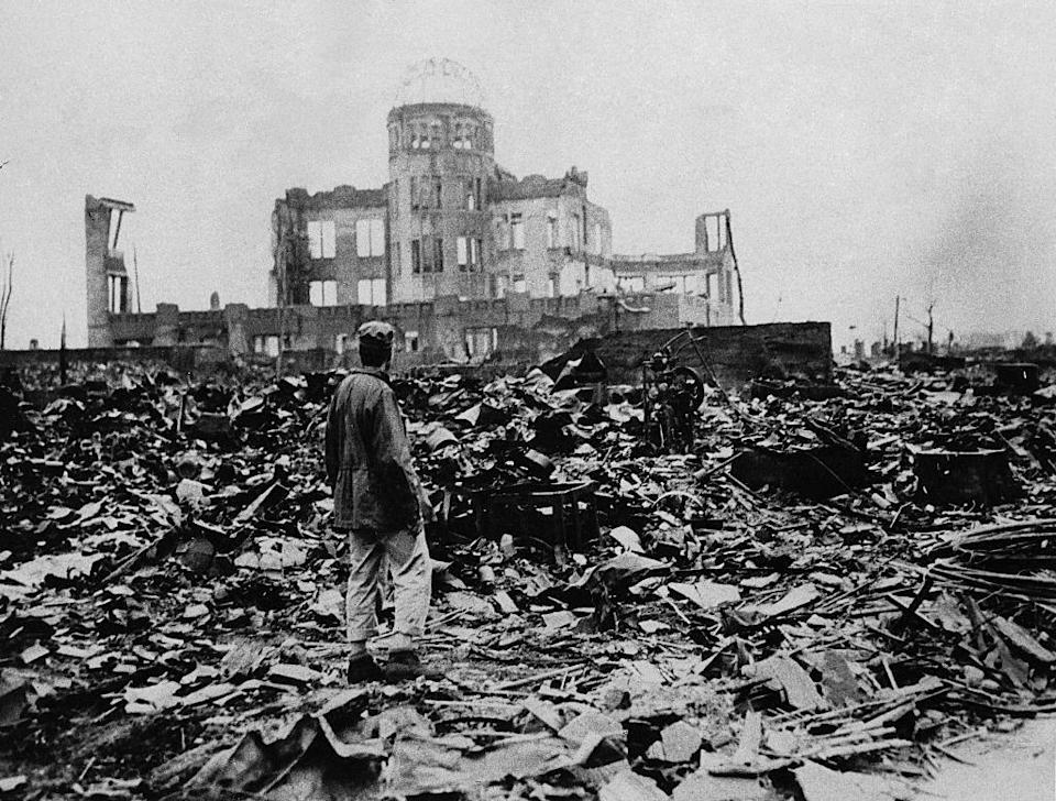 Un hombre se encuentra entre las ruinas de Hiroshima, con lo que queda de la estructura de un gran edificio frente a él, después de que una bomba atómica fuera lanzada allí.