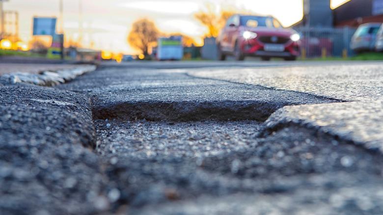A pothole in a road with a car in the background