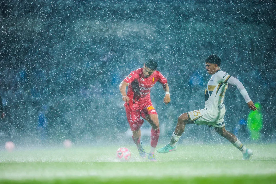 Two soccer players vie for the ball during a match in a rain storm.