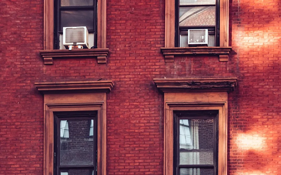Urban brick building facade with windows, including air conditioning units, and unique light patterns on the wall
