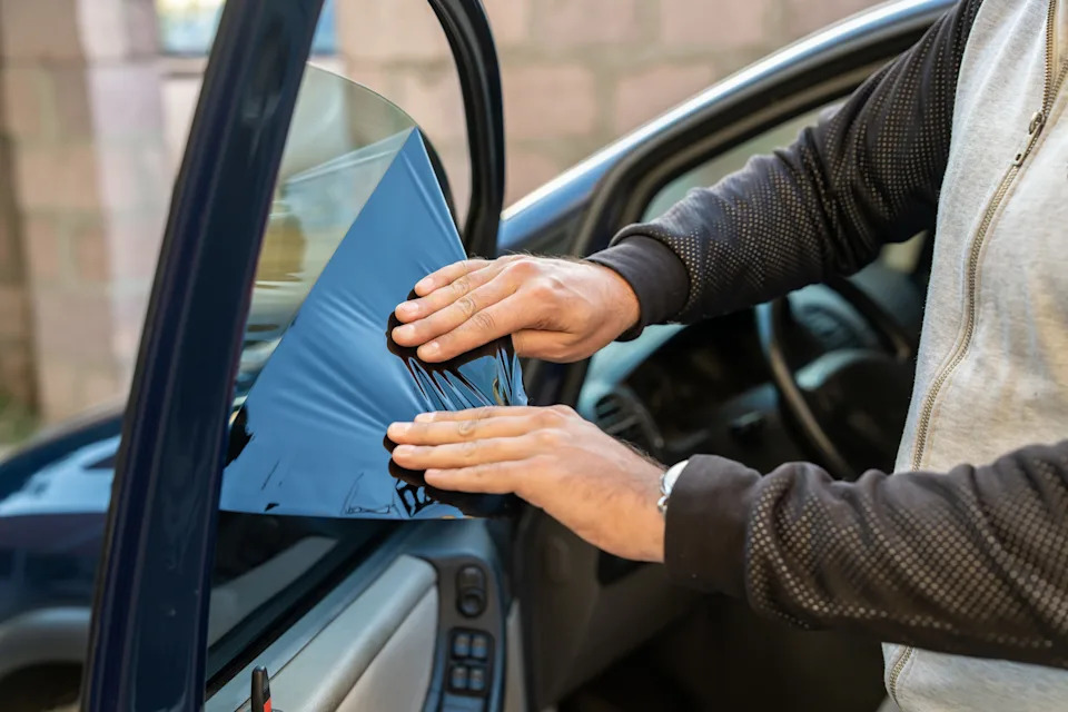 A man removes the tint from the side windows of a car.