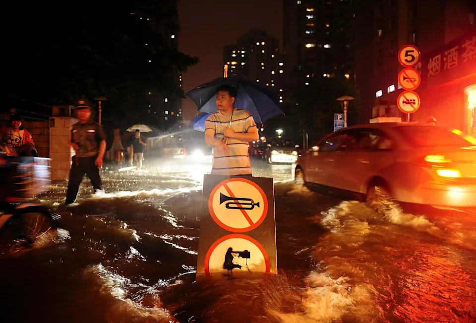A man uses a signboard to signal motorists driving through a flooded street in China.