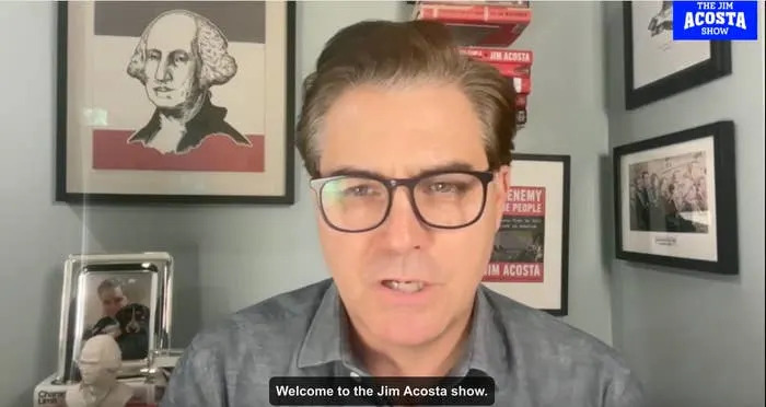 Man in glasses speaks in front of books and framed pictures, with text on screen saying "Welcome to the Jim Acosta Show."