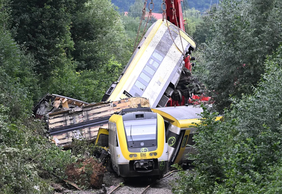 A crane works to lift a car that is part of a train wreck.