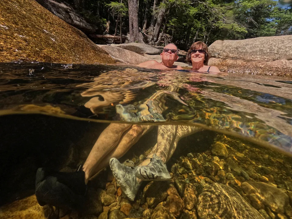 Two people sit side-by-side in a pool of water, seen both above and below the water.