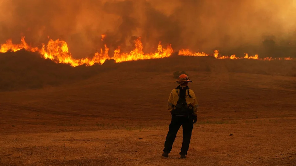 A firefighter stands and watches a wildfire burning in the background
