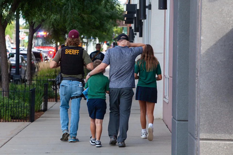 Children in Annunciation School uniforms walk with police and a parent after a man killed two children and injured several others Wednesday, Aug. 27, 2025 in Minneapolis. (Photo by Nicole Neri/Minnesota Reformer)