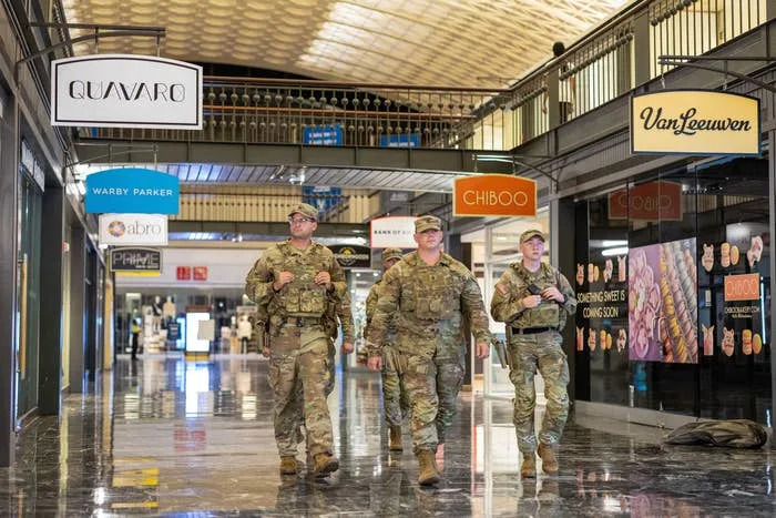 Three uniformed soldiers walking in an indoor shopping area, surrounded by various store signs