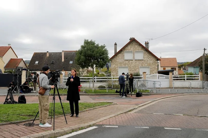 Reporters with cameras set up outside a house, conducting interviews and filming in a suburban neighborhood