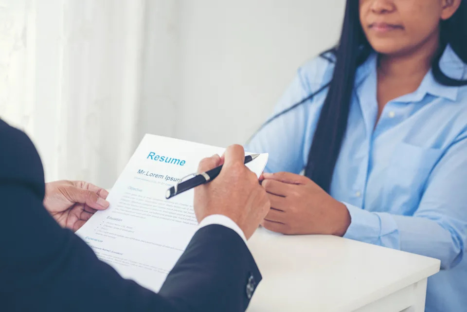 Person reviews a resume at a desk during a job interview, highlighting a common hiring process scenario