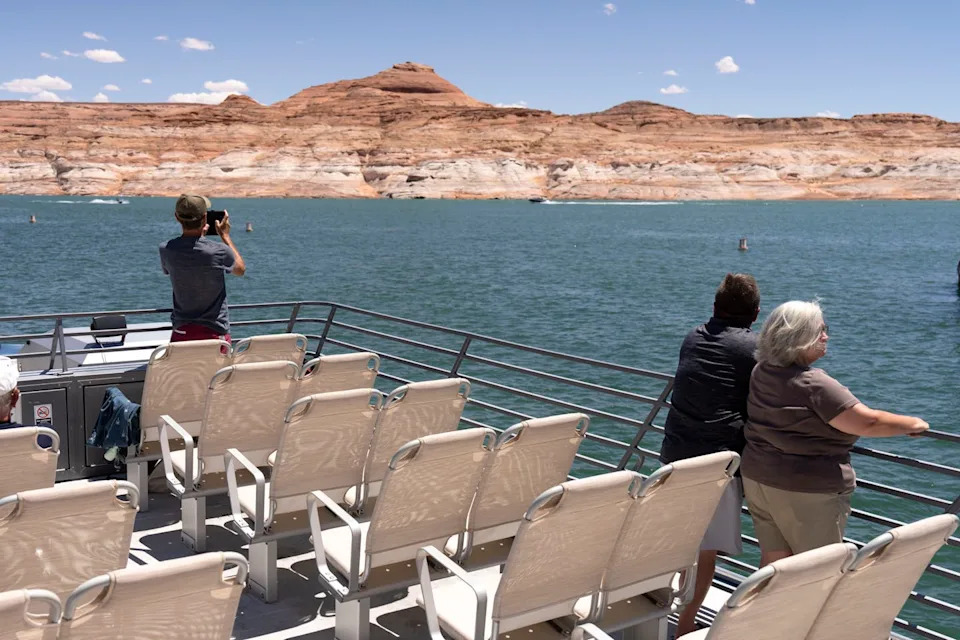 People stand on a boat looking at a body of water and mountains beyond.