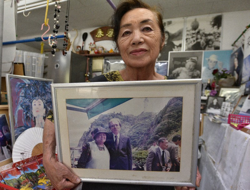 「ひばりグッズ」で埋まった店内でパネルを掲げる荒木澄江さん。パネルの写真には母の鈴木フクさん(左)の肩を抱く星野哲郎さんが写っている=福島県いわき市平薄磯で2025年6月27日午後2時26分、柿沼秀行撮影