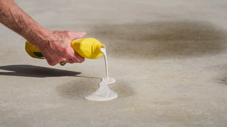 A man's arm squeezing a bottle of concrete cleaner onto an oil-stained driveway