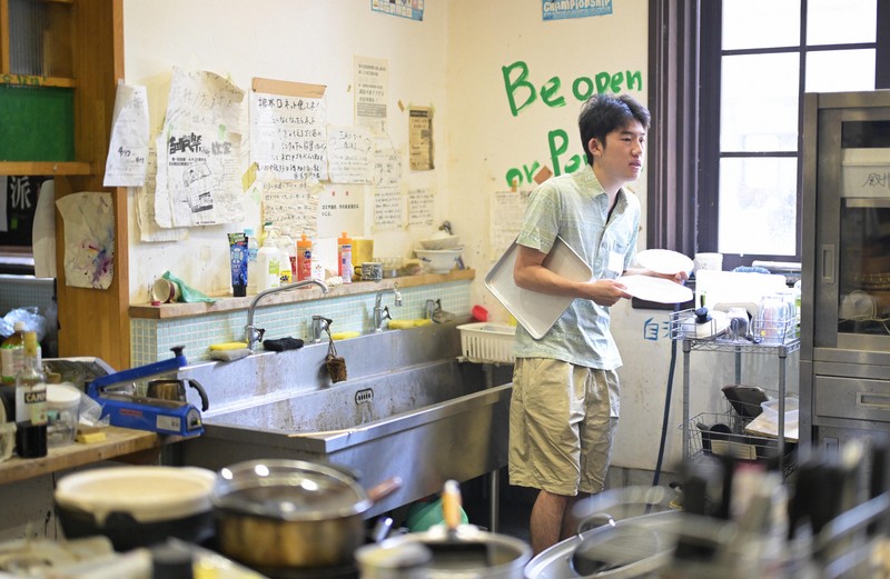 京都大学吉田寮の食堂の調理場で、水切りかごから食器を棚へ運ぶ藤田昂太郎さん。「自分がよく使わせてもらっているものだから」と話し、他の寮生が使ったものでも率先して元にあった場所へ戻していた＝京都市左京区で2025年8月1日、山崎一輝撮影