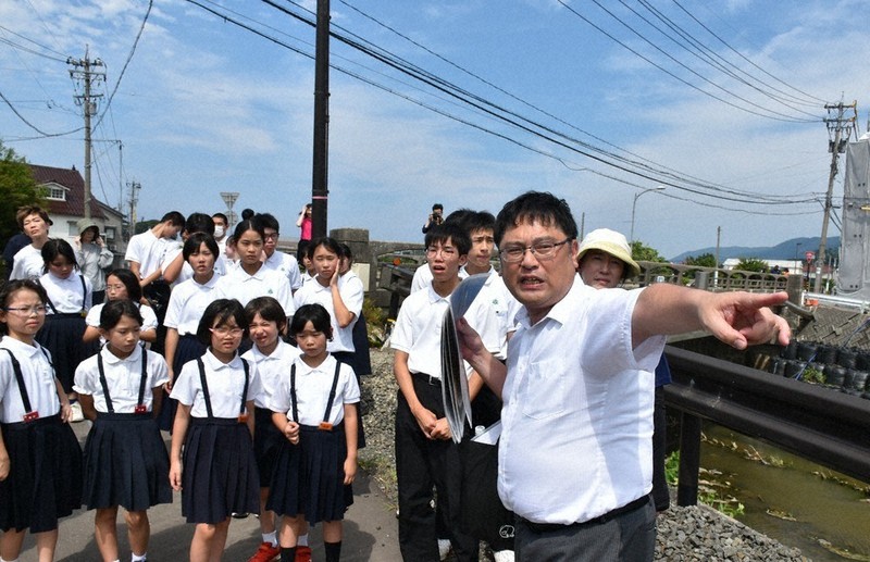 輪島中の山田忠和PTA会長（右端）の案内で、輪島市鳳至川沿いの震災と豪雨からの復旧状況を学ぶ白嶺小中の子どもたち＝輪島市で、2025年8月4日午後1時42分、中尾卓英撮影