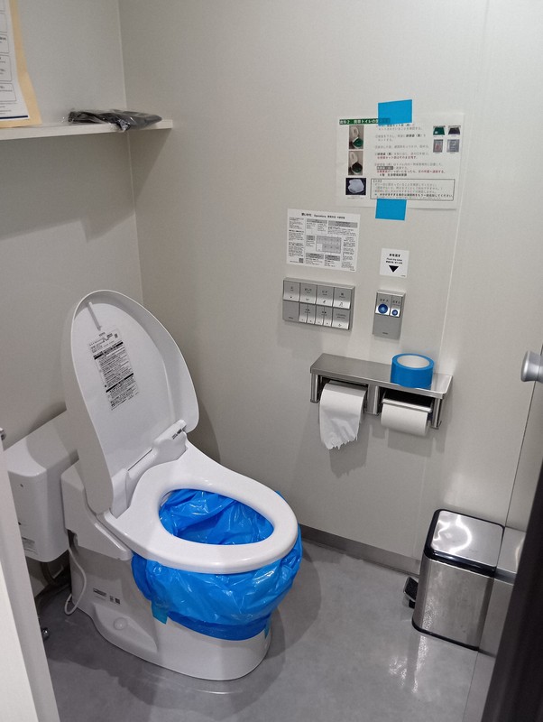 地震など災害発生時でも使えるよう、ポリ袋がかぶせられた便器。さらに、ポリ袋をもう1枚かぶせ、用を足すことになる。壁には使用マニュアルが貼られた＝徳島市万代町1の徳島県庁で2025年8月7日午後1時9分、植松晃一撮影