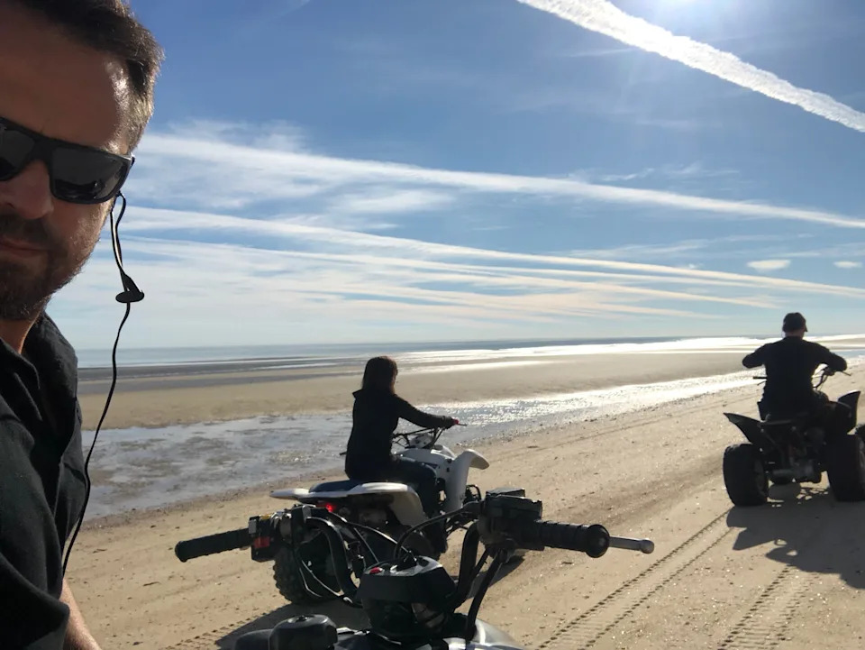 People riding ATVs on a sandy beach under a clear sky