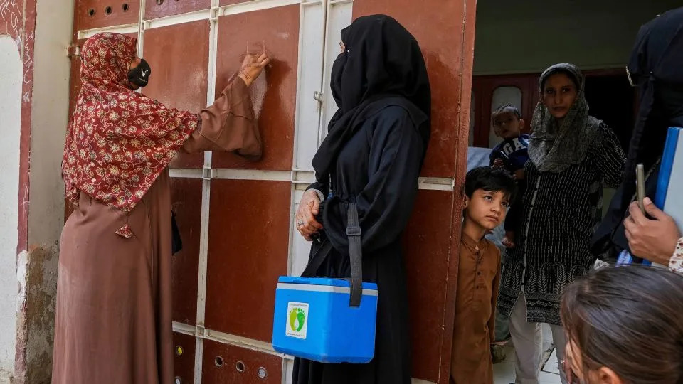 A health worker, left, marks a house after administering polio vaccines in Karachi, Pakistan, in April. - Fareed Khan/AP