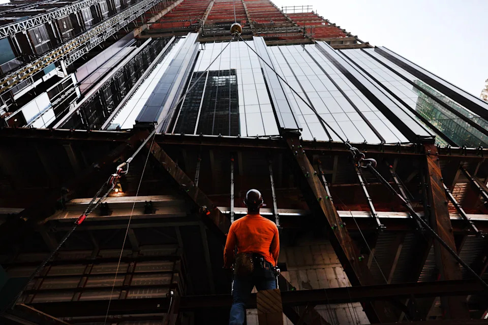 A construction worker looks up at a skyscraper