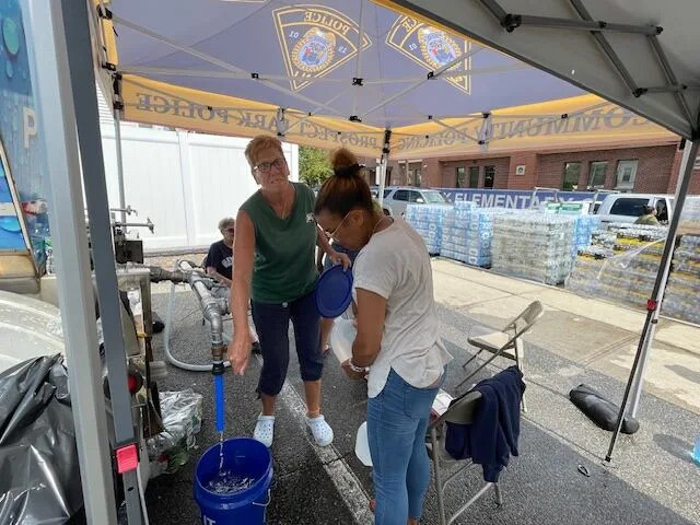 Volunteers Ruth Birch (left) and Liz Rodriguez Smith filling up a water bucket at the distribution center at the Prospect Park municipal building. Prospect Park, with about 6,000 residents, has distributed an average of 22 pallets of bottled water a day and 4,000 gallons of potable water a day, volunteers said.