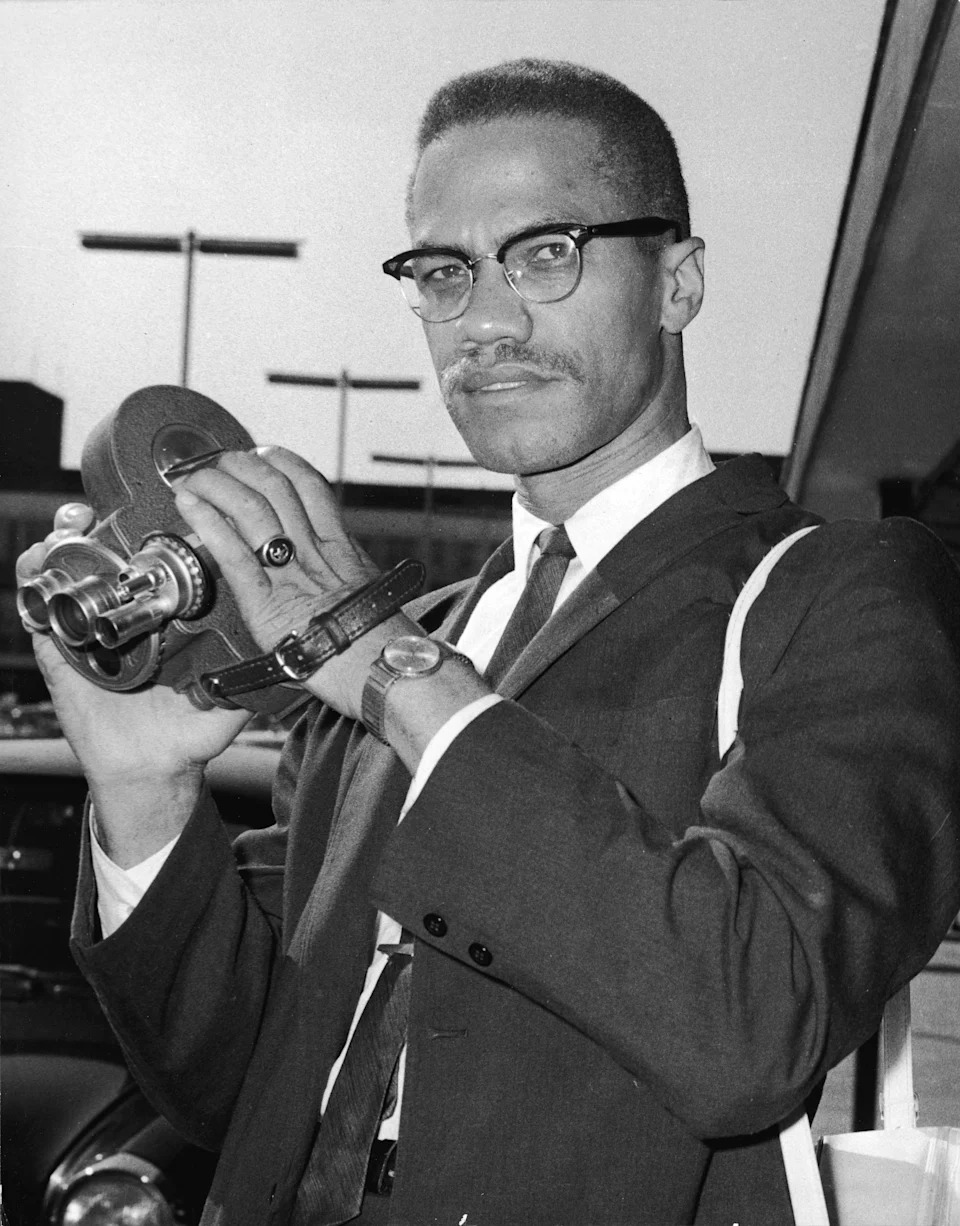 Person in a suit holds a movie camera confidently in an outdoor setting