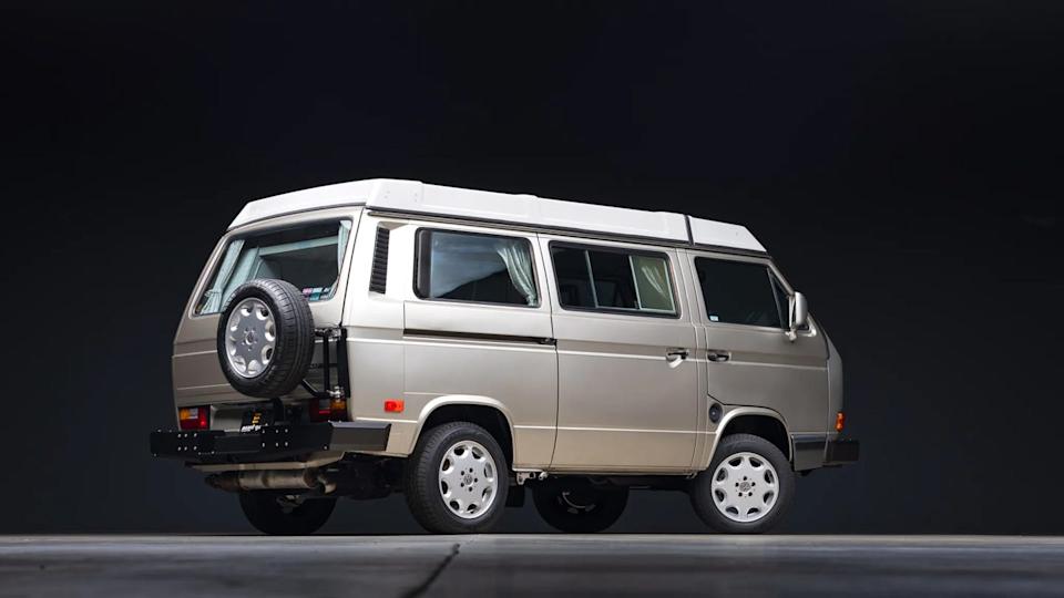 rear three quarter view of beige van with rear mounted spare tire and curtains inside windows.