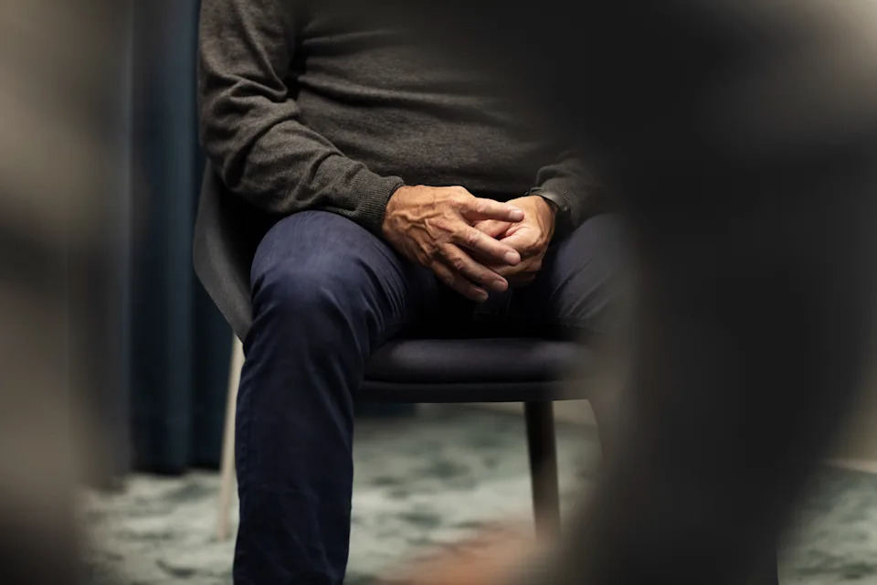 Person wearing a sweater and pants, seated with hands clasped, suggests a focused or contemplative moment during a professional setting