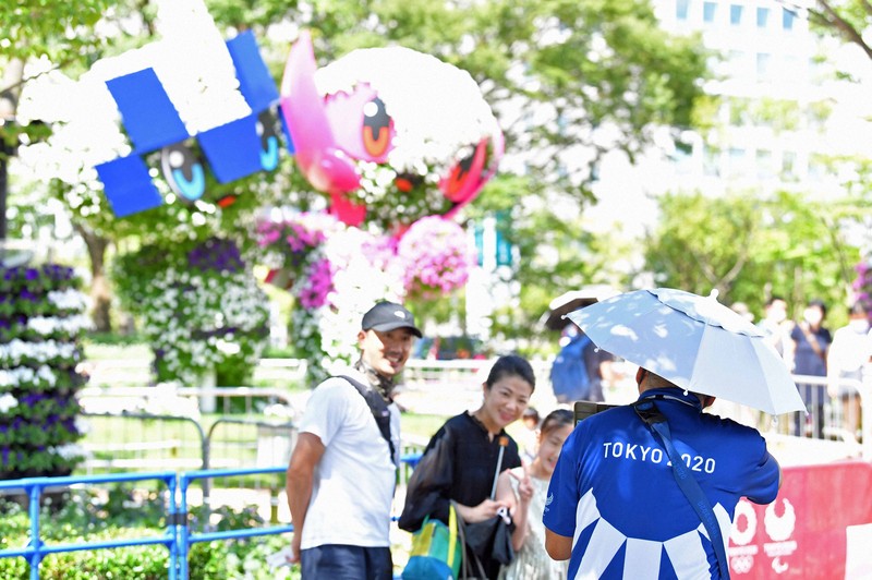 東京オリンピック・パラリンピックの競技会場近くで、「かぶる傘」をつけて家族連れの写真を撮る大会ボランティア＝東京都江東区で2021年7月25日午前9時58分、平川義之撮影