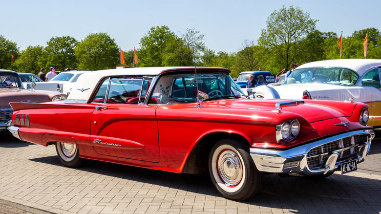 A red 1960 Ford Thunderbird with a white roof parked outdoors on a sunny day.