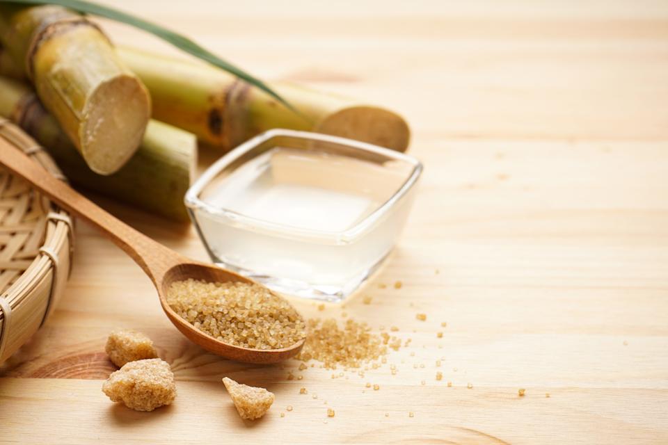 Sugarcane, fresh cane juice and brown sugar on a wooden background, space for text.