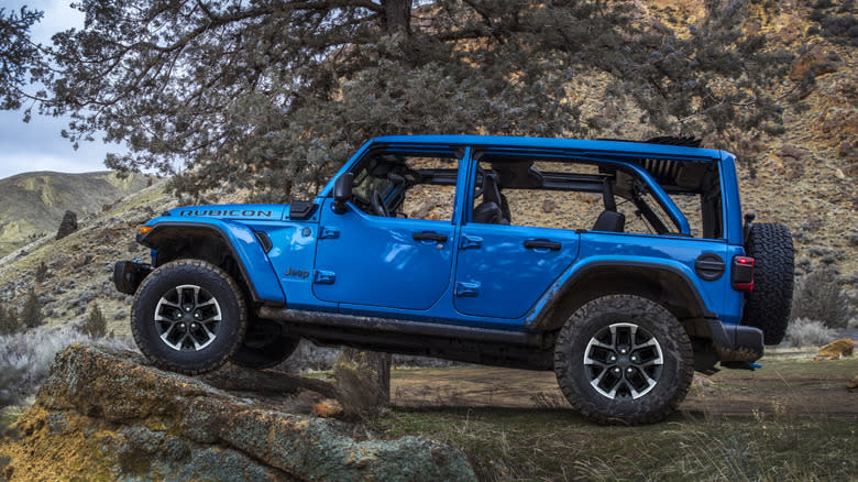 a blue Wrangler 4xe perched on a rock in front of trees and mountains